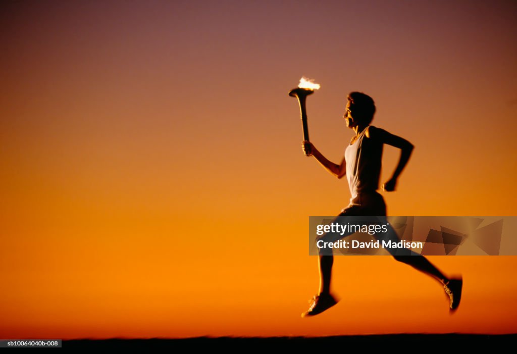 Silhouette of man running with torch at sunset