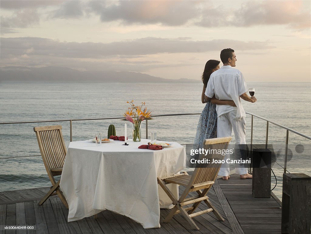 Couple in outdoor restaurant, embracing and looking at sea, side view