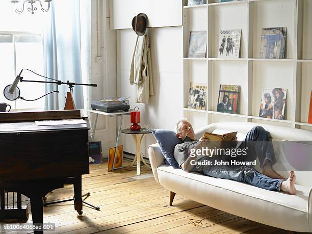 mature man lying down, reading - music home stock-fotos und bilder