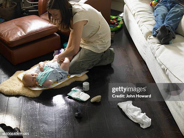 mother changing baby boy (9-12 months) on floor, father on sofa - nappy change stockfoto's en -beelden