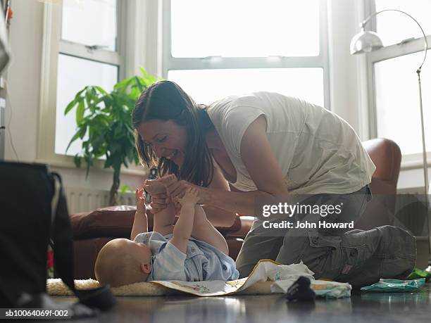 mother changing baby boy (9-12 months) on floor - nappy change stockfoto's en -beelden