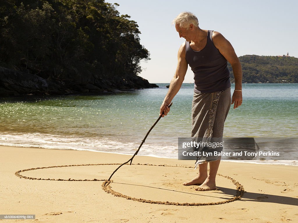 Mature man drawing heart on sand