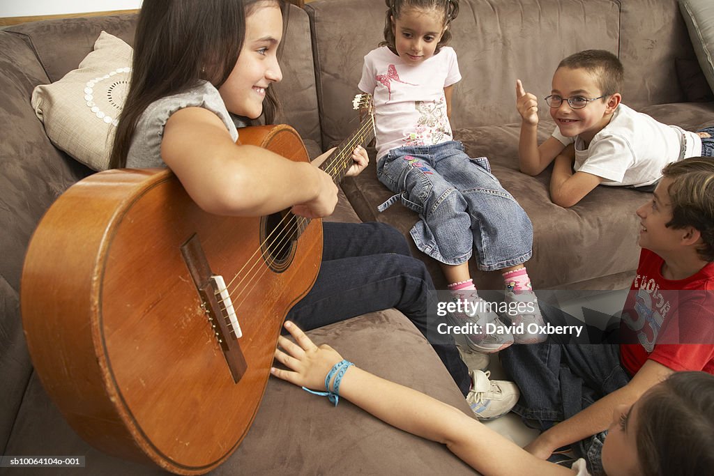 Group of children (7-10) relaxing on sofa, girl playing guitar