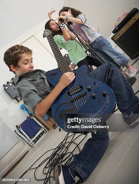 boy (10-11) playing guitar, girls (6-7) singing in garage - child rock band stock-fotos und bilder