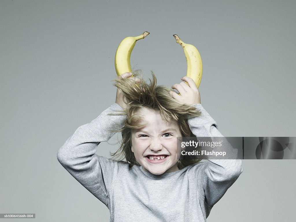 Boy (6-7) holding two banana on head, smiling, close-up