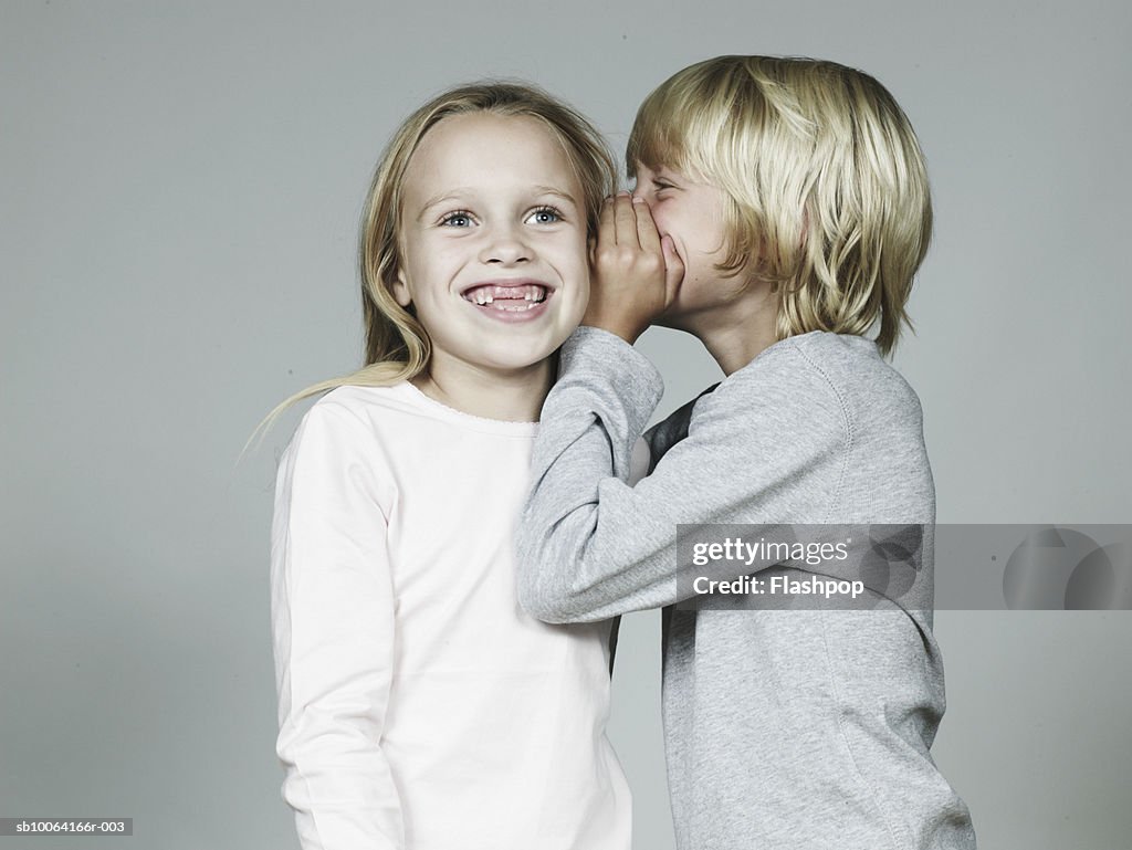 Boy (8-9) whispering in girl (6-7) ear, smiling, close-up