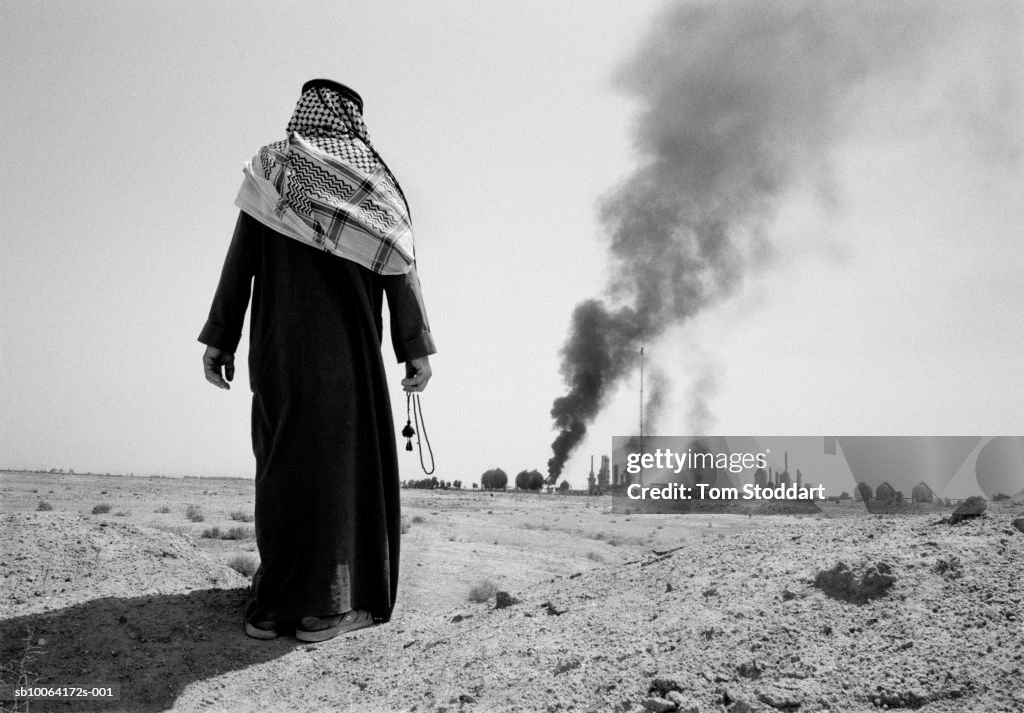 Man watching burning petrochemical plant, rear view (B&W)