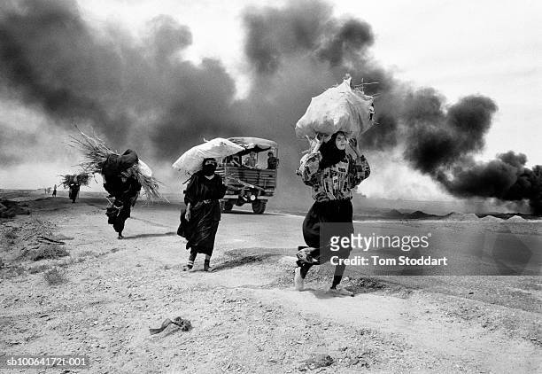 , Iraqi women carrying firewood walk through thick smoke from burning oil in an oil field near Basrah, Southern Iraq a week after British troops...