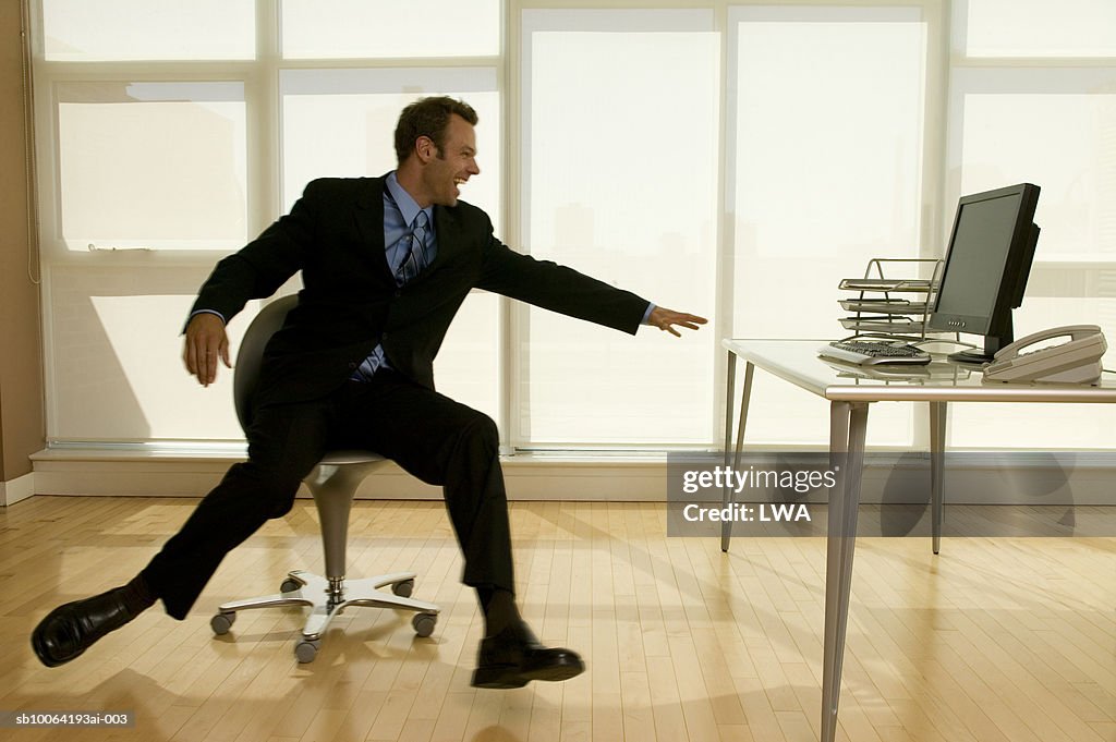 Businessman sitting on chair reaching at table, laughing