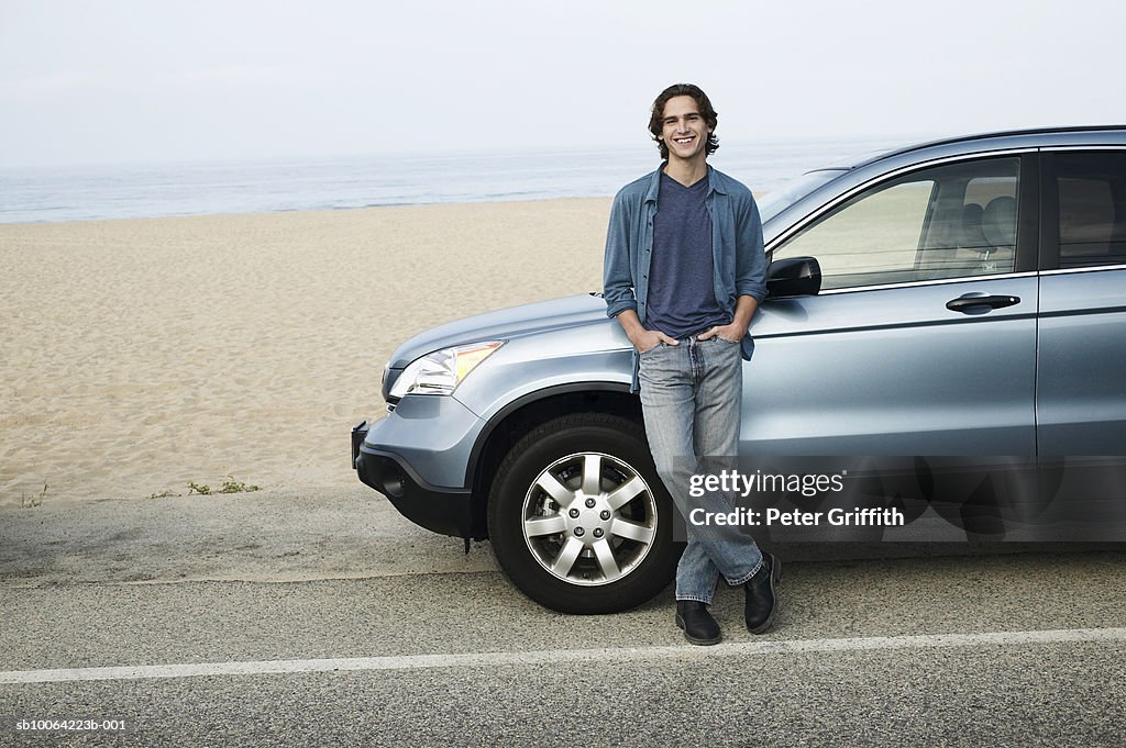 Man leaning against parked car next to beach, portrait