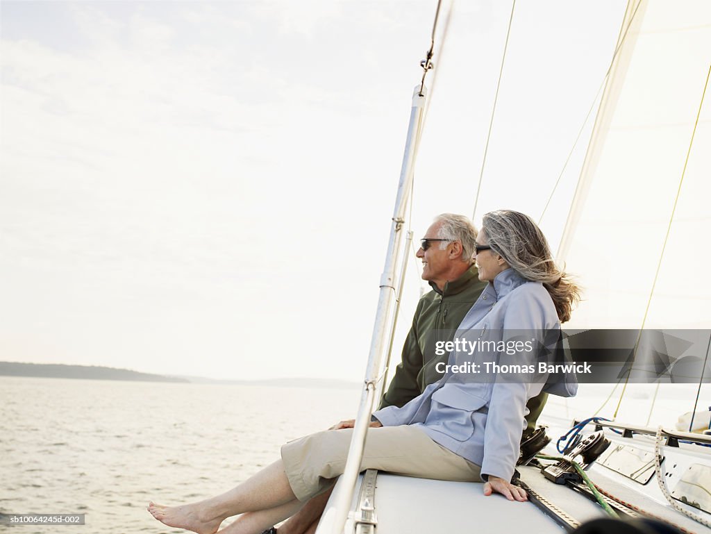 Mature couple sitting at bow of sailboat, looking at view, smiling