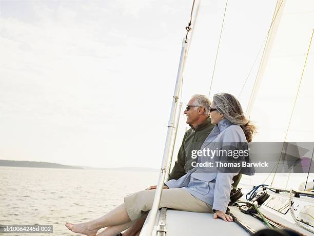 mature couple sitting at bow of sailboat, looking at view, smiling - sailing couple stock pictures, royalty-free photos & images