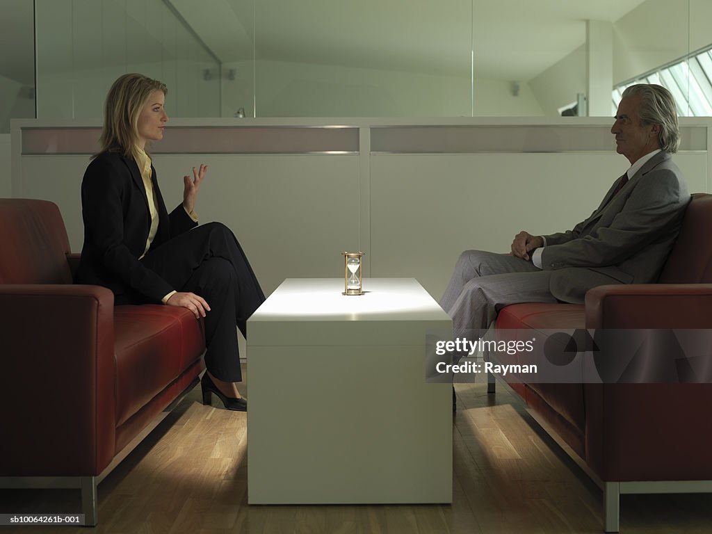 Business man and woman having conversation, hourglass on table