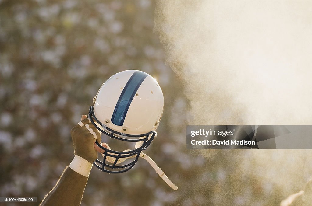 Football player waving helmet in air.