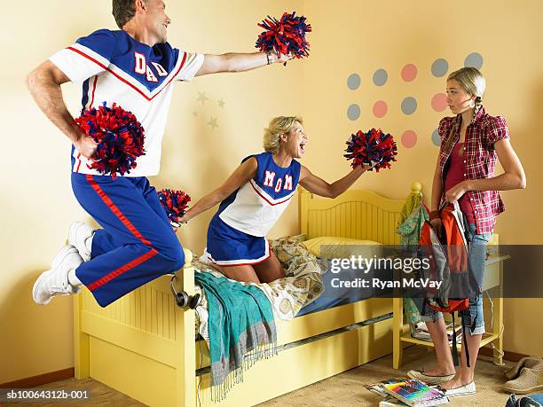 mother and father dancing with pom poms looking at daughter (13-14) - teen cheerleader stock-fotos und bilder