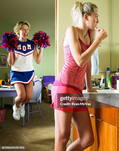mother holding pom poms and jumping, girl (13-14) brushing teeth in bathroom - teen cheerleader stock-fotos und bilder