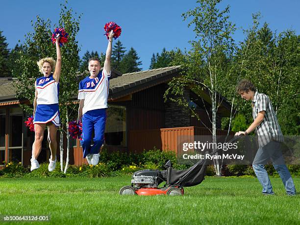 teenage boy (14-15) using lawnmower, mother and father holding pom poms and jumping - teen cheerleader stock-fotos und bilder