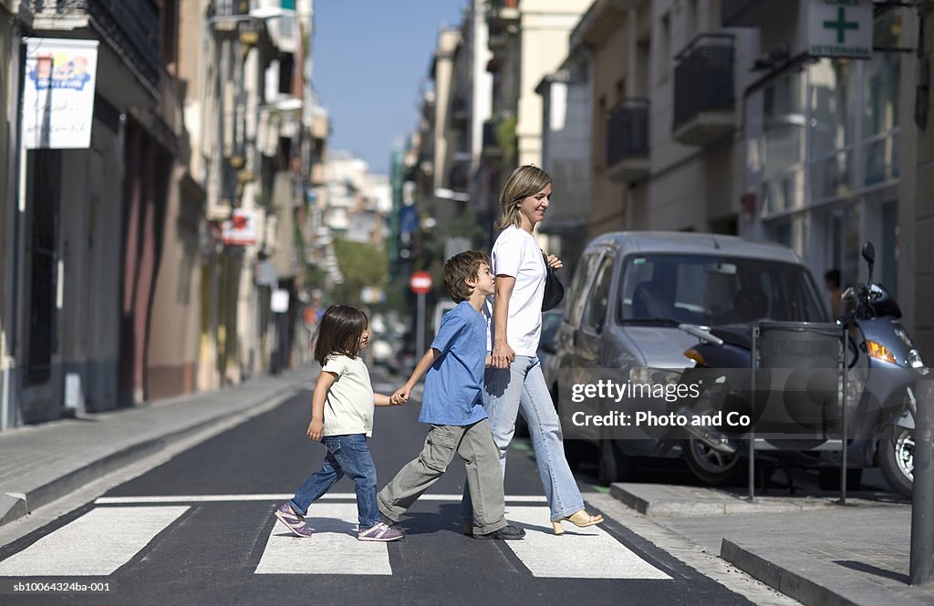 Mother with children (3-7) crossing street, side view