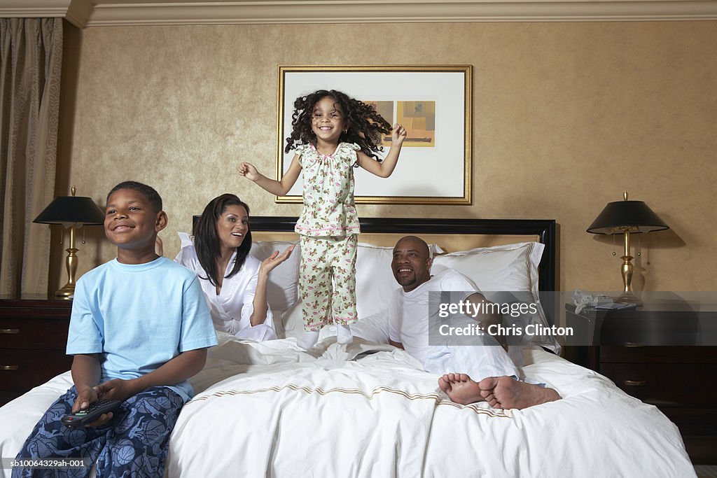 Family with two children (4-7) on bed, girl jumping