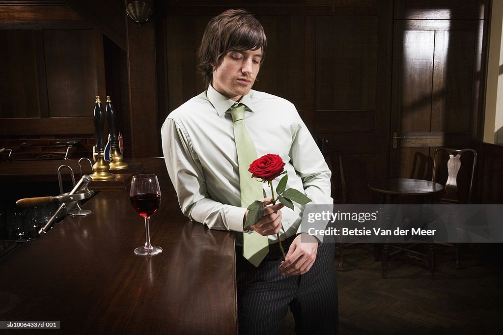 Man standing in bar looking at red rose