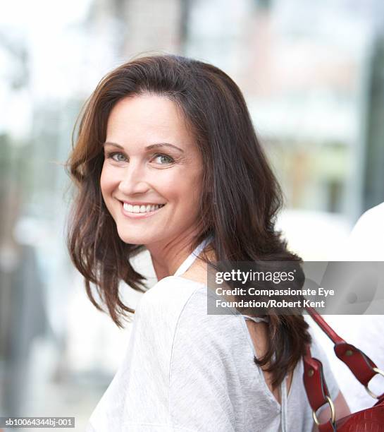 portrait of mature woman looking over shoulder, smiling - older woman with brown hair stockfoto's en -beelden