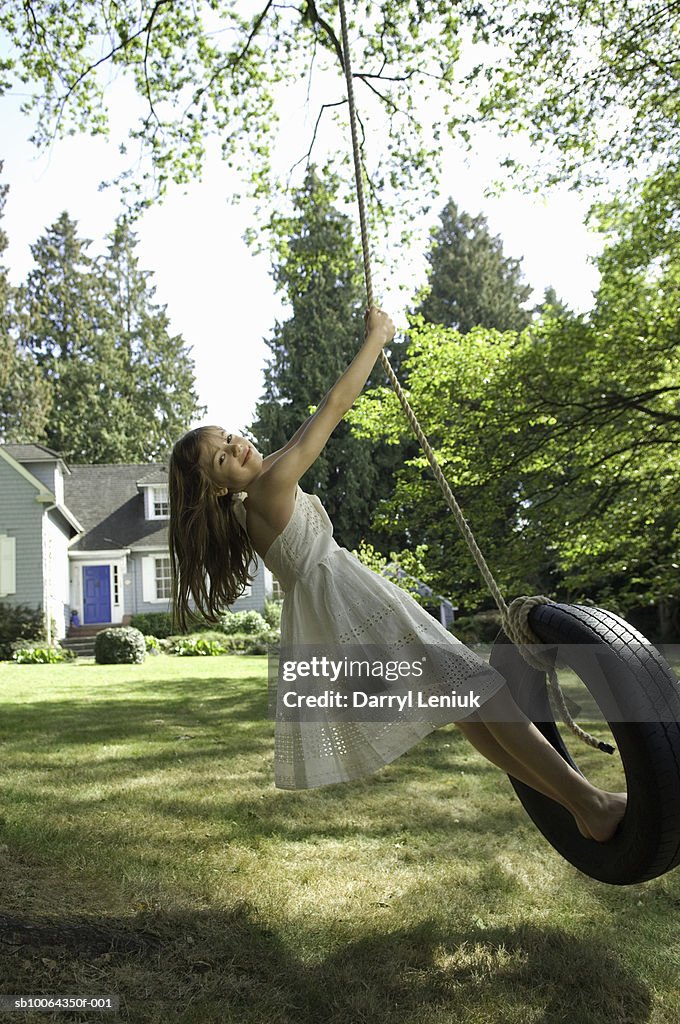 Girl (8-9) playing on tyre swing in front of suburban house, portrait