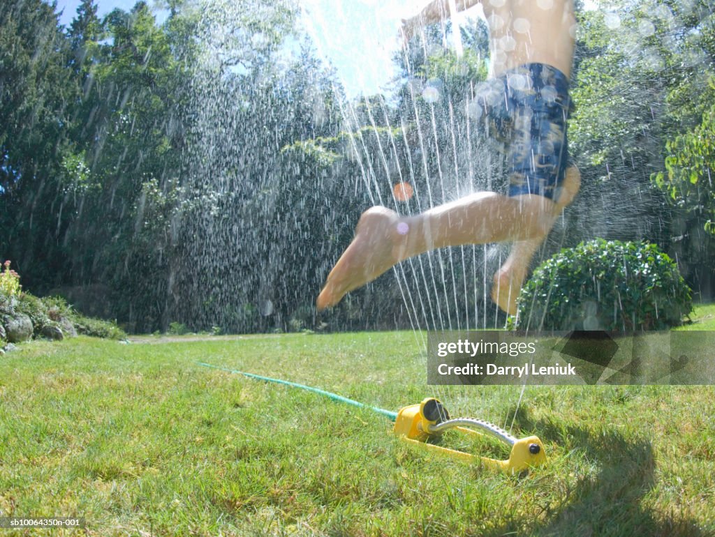 Boy (6-7) jumping through water sprinkler