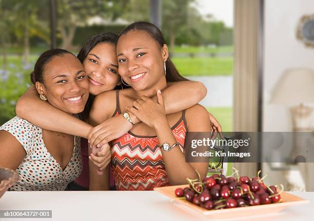 three young women sitting at table and hugging, portrait - haitian ethnicity stock pictures, royalty-free photos & images