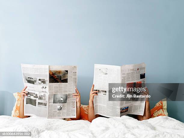 young couple reading newspaper on bed - periódico fotografías e imágenes de stock