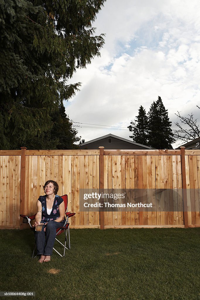 Woman sitting on chair in lawn by wooden fence