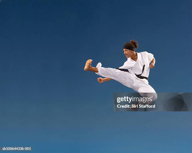 teenage boy (14-15) kicking in mid-air, low angle view - arte marziale foto e immagini stock