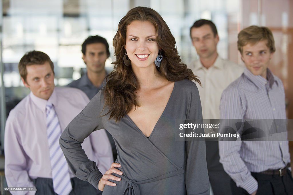 Portrait of young woman, four men in background looking at her