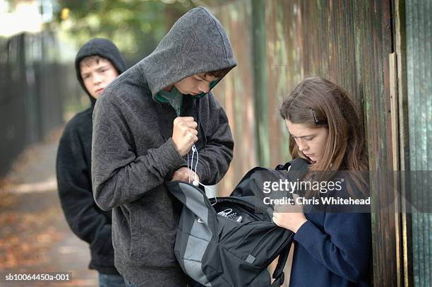 two teenage boys (14-15) in hoods stealing items from school girl's bag (12-13) - child aggression stock pictures, royalty-free photos & images