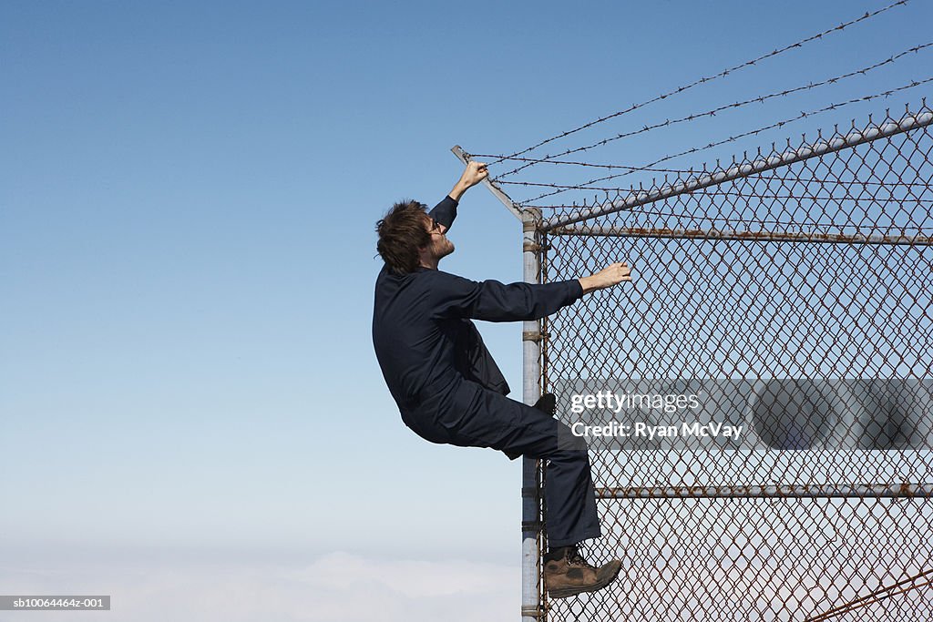 Man climbing chain link fence with barbed wire on top