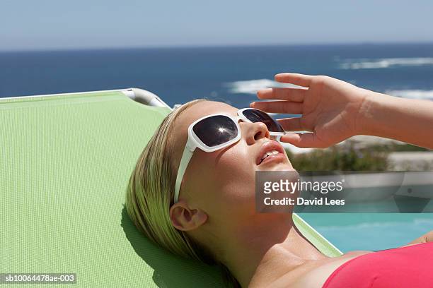young woman relaxing on sunlounger beside swimming pool near ocean - women sunbathing pool - fotografias e filmes do acervo