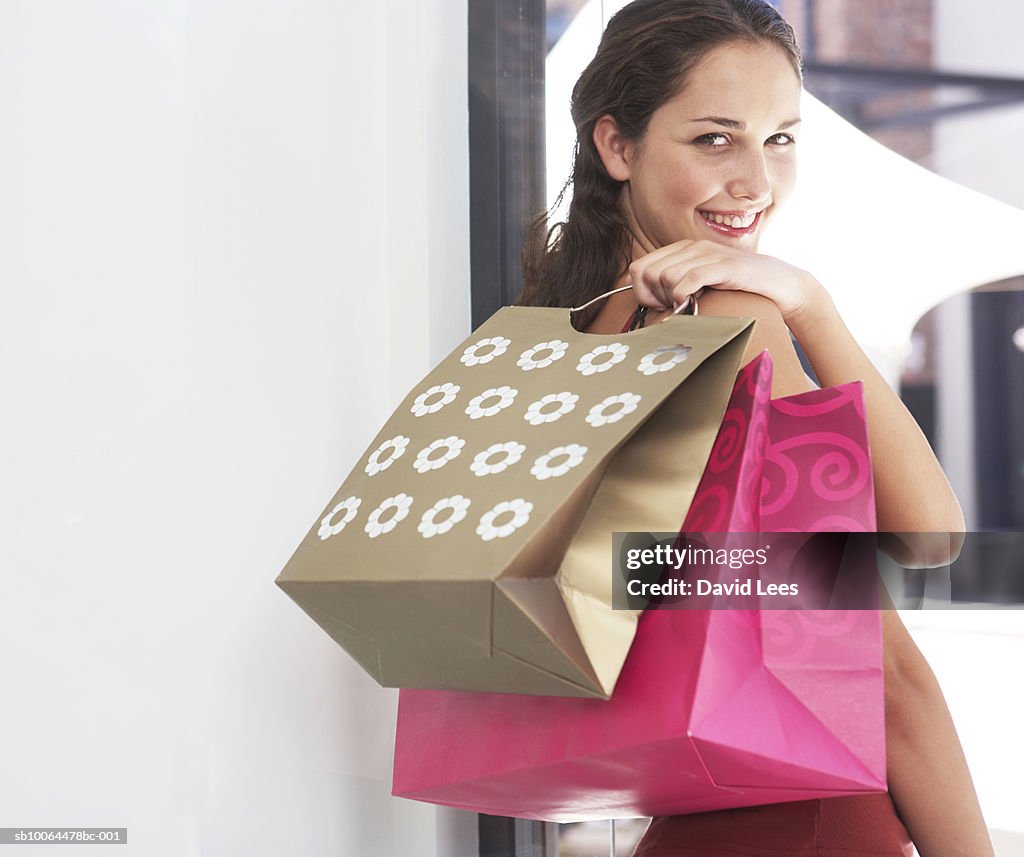 Portrait of young woman looking over shoulder, holding shopping bags