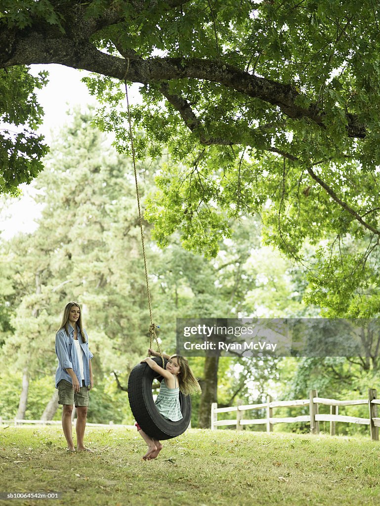 Mother watching daughter (4-5) playing on tire swing
