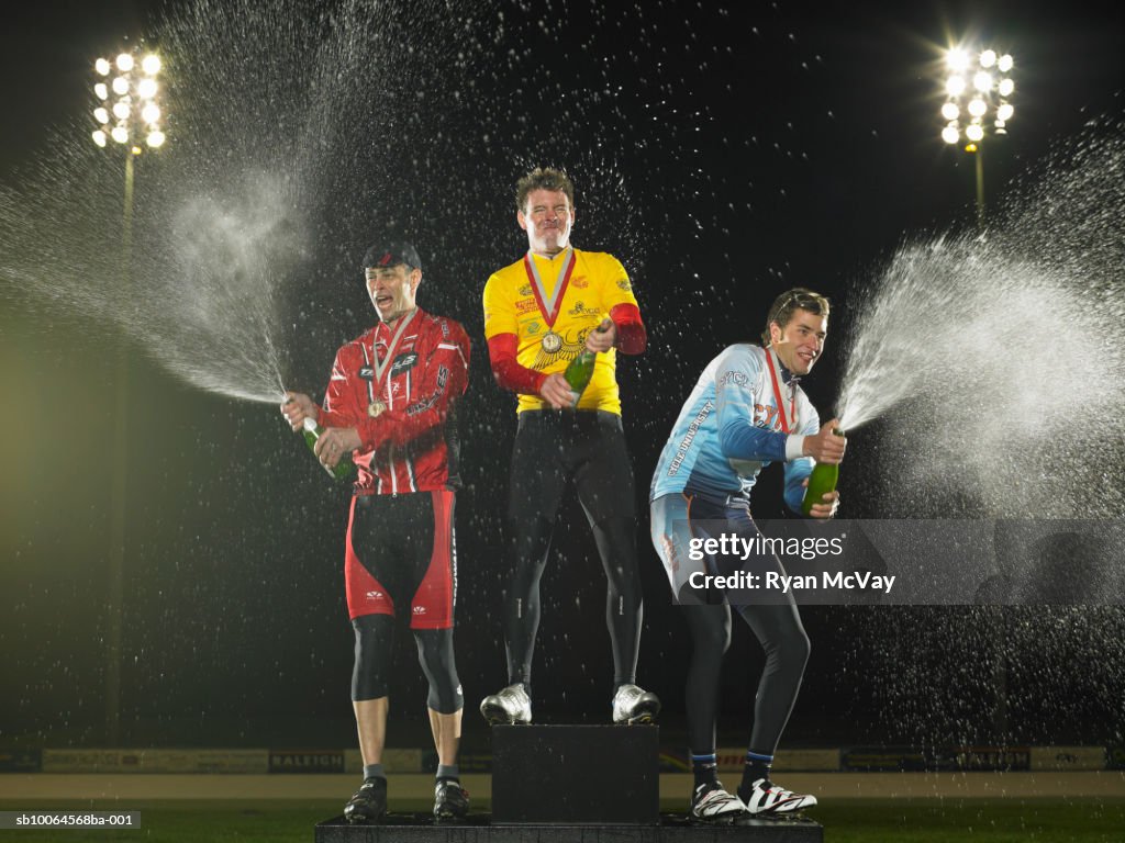 Cyclists standing on podium, spraying champagne