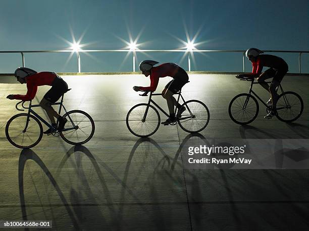 cyclists on velodrome track at night, side view - baanwielrennen stockfoto's en -beelden