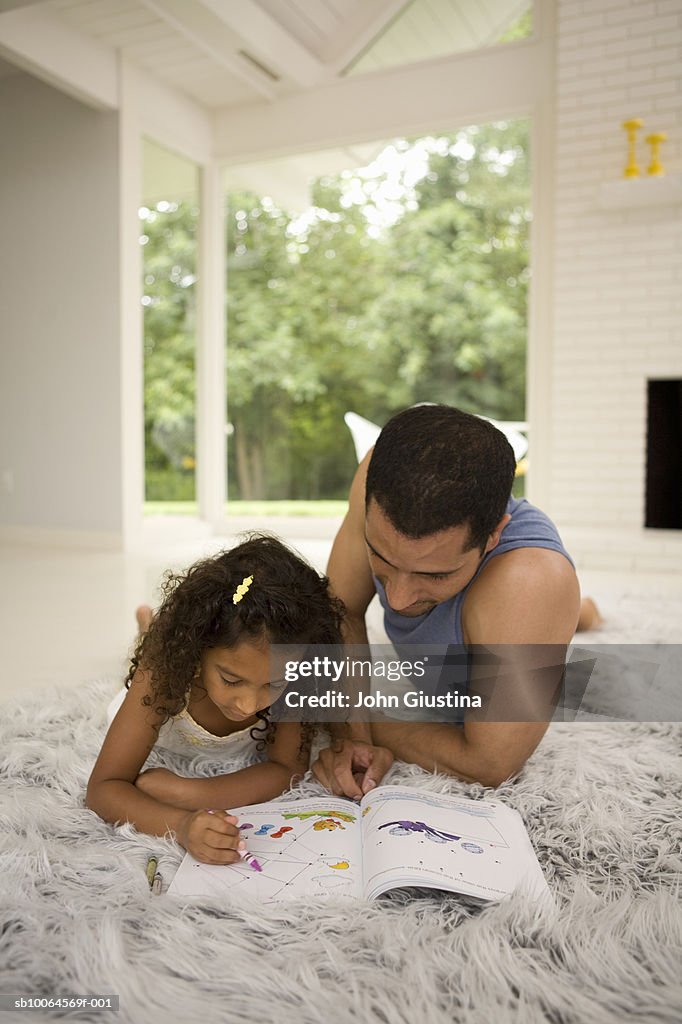 Father and daughter (6-7) lying on rug, drawing on book with crayon