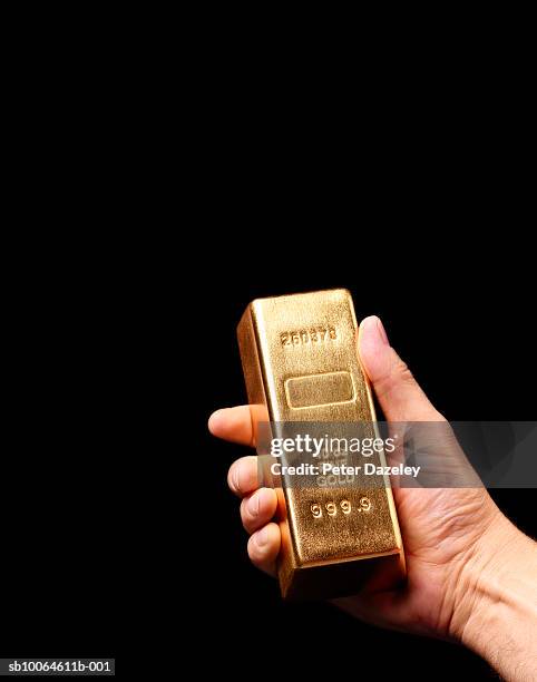 person holding gold ingot against black background, close-up of hand - barren stock-fotos und bilder