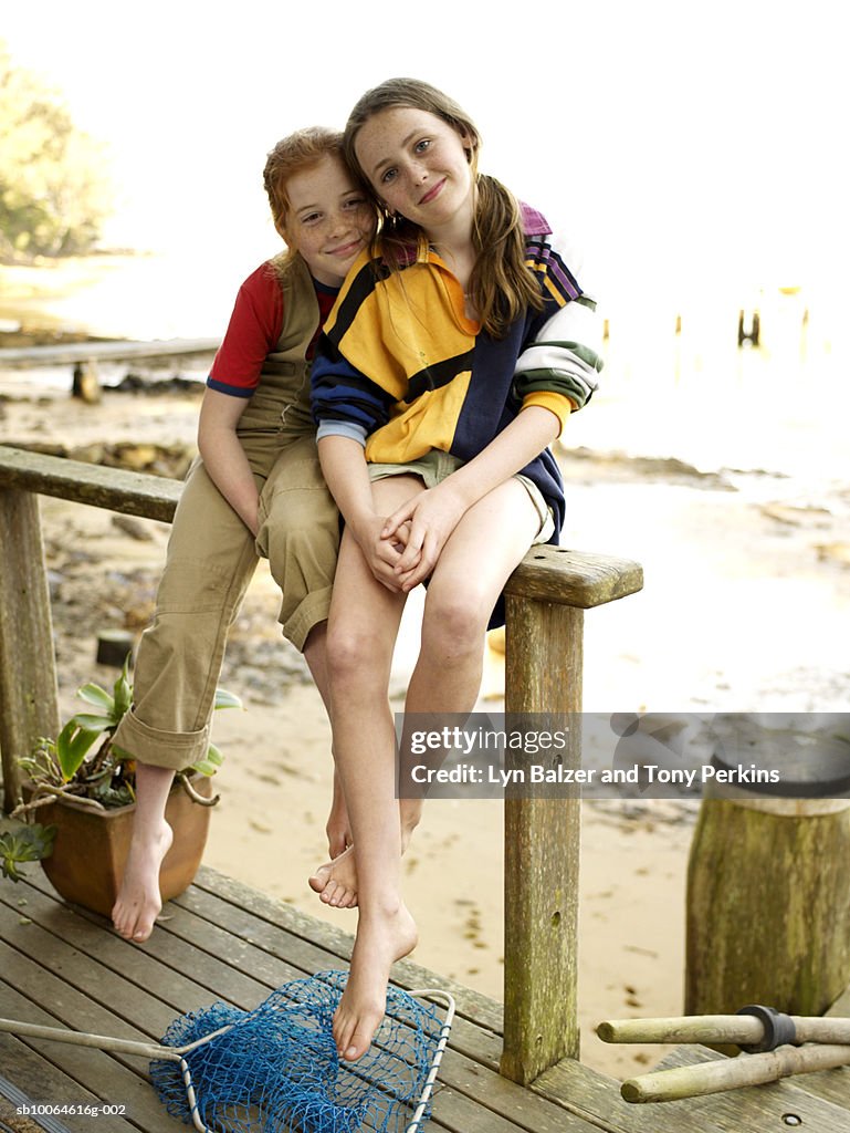 Two girls (10-11) sitting on porch railing, smiling, portrait