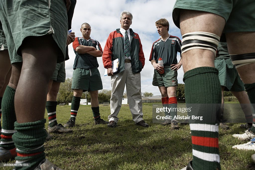 Rugby players standing around coach on lawn, low angle view