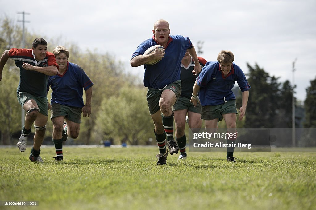 Rugby players running with ball on sports field