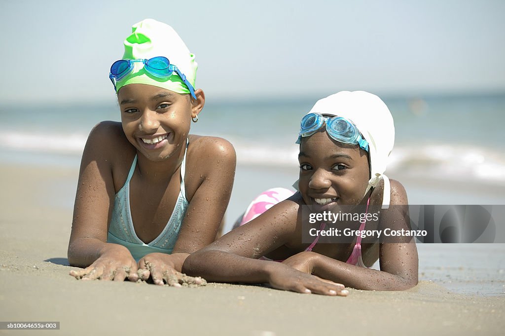 Two girls (8-9) lying on beach, smiling, portrait, (focus on foreground)