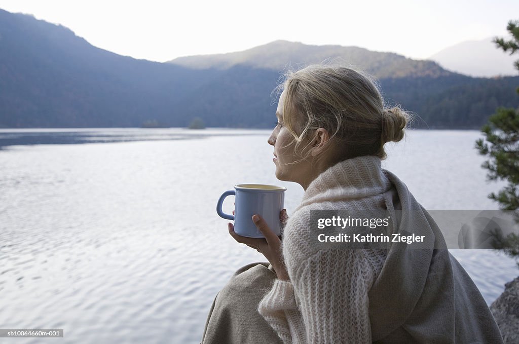 Young woman wrapped in blanket holding coffee cup