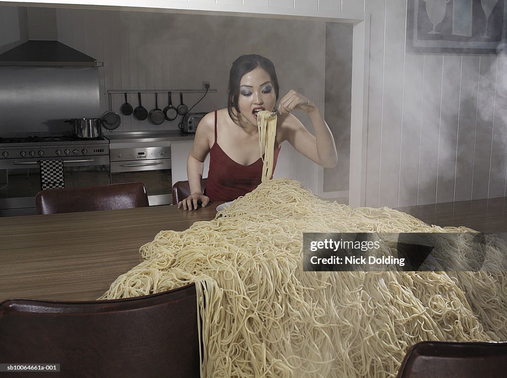 Woman standing at table eating heap of spaghetti