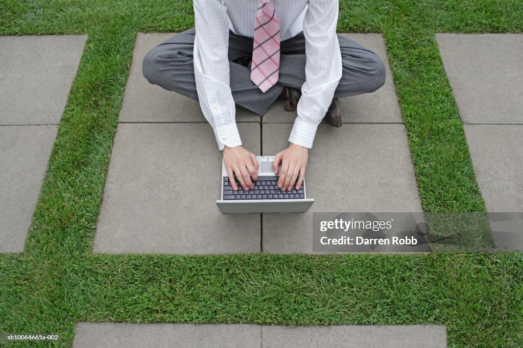 Young businessman sitting on pavement, using laptop, low section