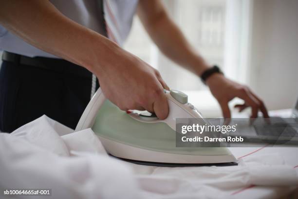 businessman ironing and using laptop, mid section, (differential focus) - strijkijzer stockfoto's en -beelden