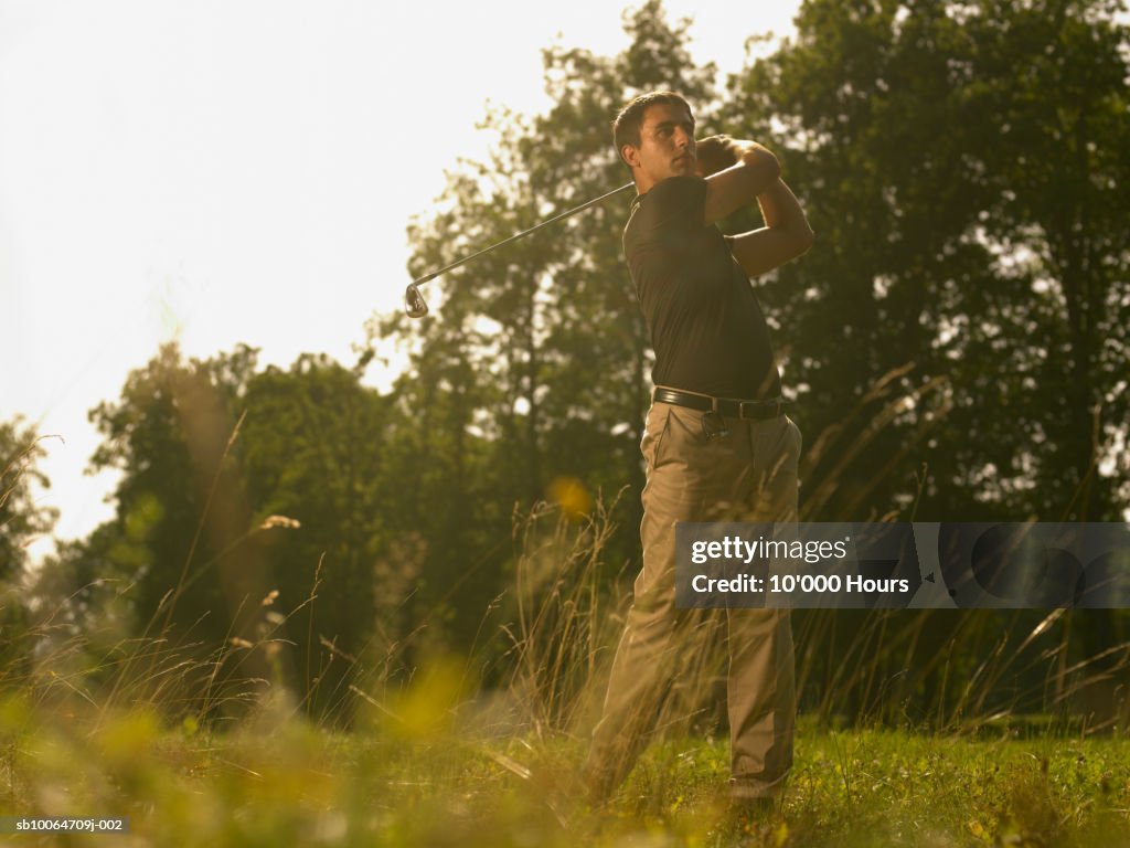 Young man playing golf, looking away (focus on background)